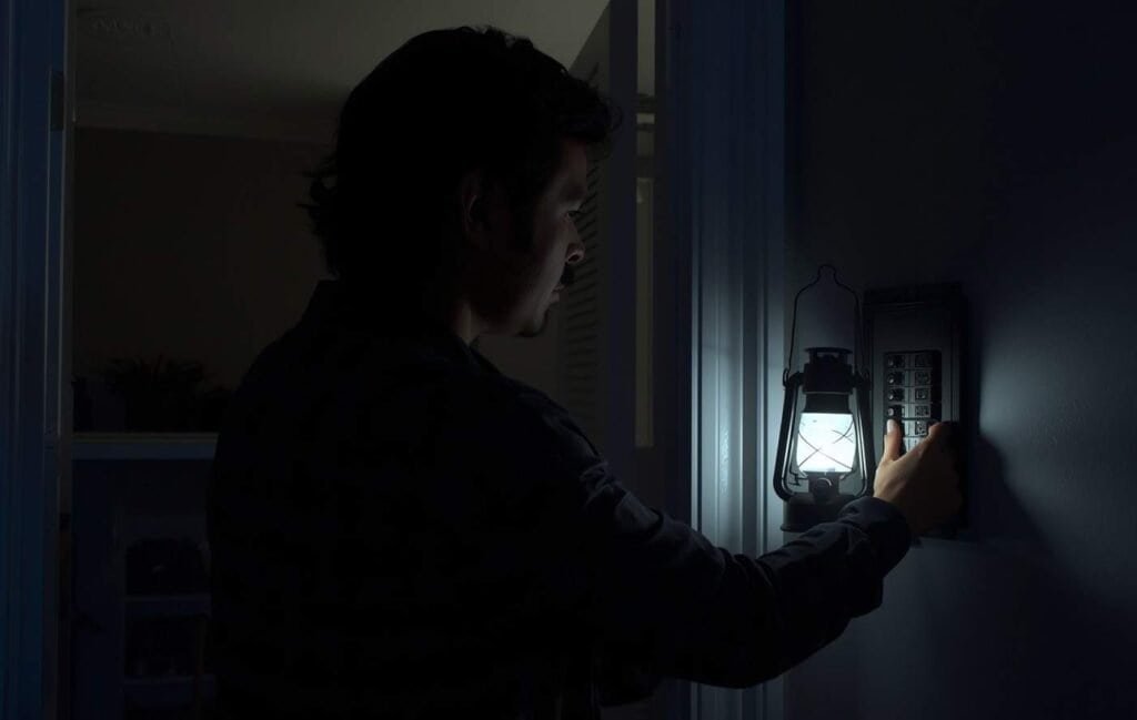 Homeowner checking circuit breaker panel using LED lantern during a nighttime power outage.